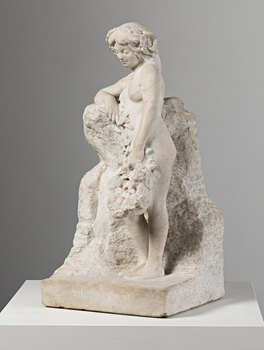 Angled view of an off-white marble statue of a naked woman with a basket of fruit loosely held in her left hand and tipping outwards over her knees. Her right arm leans on a rock. Her feet stand on a rectangular base.