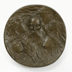 Round patinated plaster sculpture in bronze colour. Main subject is a man's face, with bald head and long flowing beard. Five female faces, with long flowing hair, surround him.