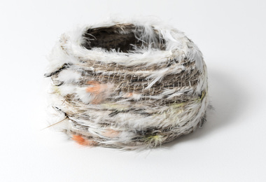 Small woven basket with rows of white feathers and spots of yellow and red feathers throughout.