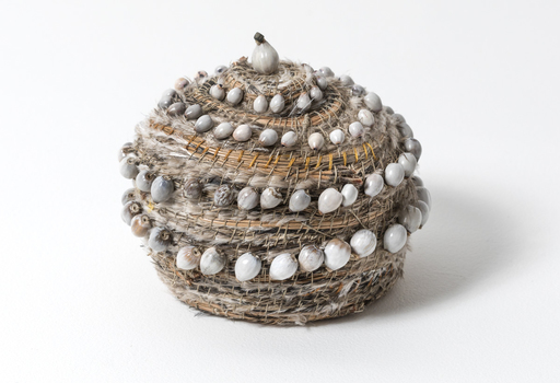 Small woven basket with lid, decorated with rows of small white and grey job seeds, feathers and pine needles.