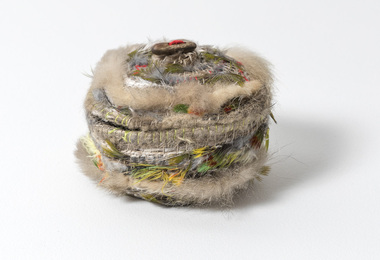 Small woven basket sculpture with lid. Basket has rows of brown emu feather and coloured peacock and parrot feathers and a brown seed lid attached with red cotton.