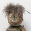 Close up photograph of the head of a woven sculpture. It has rows of feathers and raffia with brown feathers for hair and, seeds for eyes and teeth.