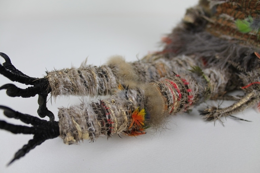 Close up photograph of the woven figure's legs and feet, made from woven feathers, cotton and raffia with crow's feet.