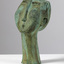 Patinated bronze sculpture with a green finish of a whistling man's head. Eyes are slits and nose is elongated.