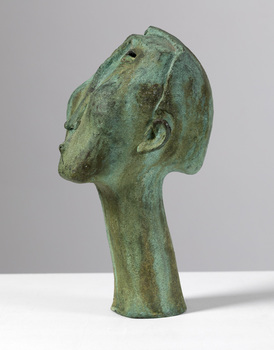 Side angle of a patinated bronze sculpture with a green finish of a whistling man's head. Eyes are slits and nose is elongated.