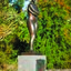 Photograph of an outdoor sculpture of a female, cast in bronze. Figure has crossed arms and is wearing bathers and a swimming cap. Stands on a polished granite pedestal, to which is affixed a low relief bronze sculptural panel.