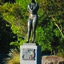 Photograph of an outdoor sculpture of a female, cast in bronze. Figure has crossed arms and is wearing bathers and a swimming cap. Stands on a polished granite pedestal, to which is affixed a low relief bronze sculptural panel.