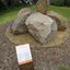 Photograph of an outdoor sculpture comprising of a group of six large bluestones laid on crushed yellow ochre sandstone surrounded by grass and distant vegetation.