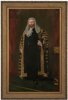 Formal portrait of a standing man in ceremonial robes of Parliamentary Speaker standing on the dais beneath the canopy of the Legislative Assembly Chamber. He wears black silk and gold laced robe, over a three piece black suit, laced jabot and cuffs, black buckled shoes, and a ceremonial long wig. Housed in a thick gilt frame of running oak leaf pattern.