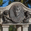 Detail of an oval bronze relief medallion of a woman, from shoulders up flanked by 2 cherubs.  The medallion is attached to a granite canopy which sits on four small plinths. 