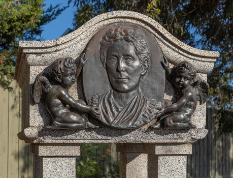 Detail of an oval bronze relief medallion of a woman, from shoulders up flanked by 2 cherubs.  The medallion is attached to a granite canopy which sits on four small plinths. 