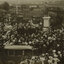 A large group of people surrounding the large bronze statue of Sir Thomas Bent which stands on a tall granite pedestal. On the left of this is another smaller memorial which is covered by a cloth. In the foreground is an early 20th century car. Paddocks and houses can be seen in the distance.