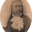 Oval shaped sepia toned portrait photograph of a bearded man from chest up, he is wearing a white wig and a lace jabot at front of a dark suit.