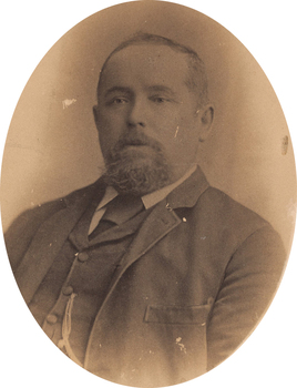 Oval shaped sepia toned portrait photograph of a man from chest up with a receding hairline, a goatee, and wearing a suit with a tie