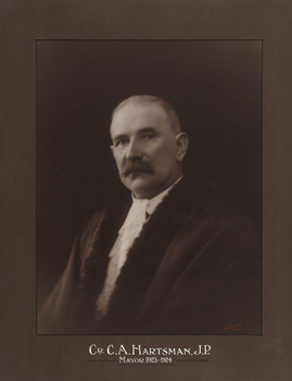 Sepia photograph of a formal portrait of a seated man, chest up, wearing mayoral robes with fur trims and jabot. 