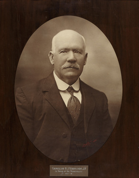 Oval shaped sepia photograph of a formal portrait of a seated man, chest up, wearing jacket, waistcoat, collared white shirt, patterned tie
