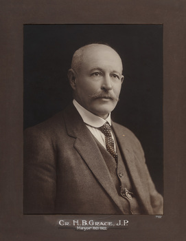 Sepia photograph of a formal portrait of a seated man, chest up, wearing three piece grey suit, white collared shirt and patterned tie.