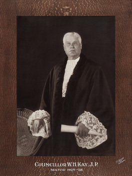 Sepia photograph of formal portrait of standing man with white hair wearing mayoral robes with fur trims and lace cuffs and jabot.
