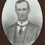 Black and white photograph of an oval portrait of a suited man with dark hair.