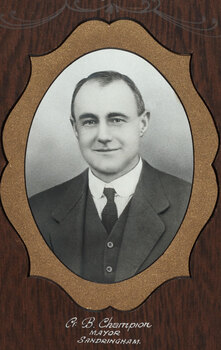 Black and white photograph of an oval portrait of a suited man with dark hair, surrounded by gold border