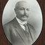 Black and white photograph of an oval portrait of a suited man with balding grey hair and moustache