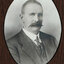 Black and white photograph of an oval portrait of a suited man with balding hair and moustache
