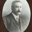Black and white photograph of an oval portrait of a suited man with darkhair and moustache