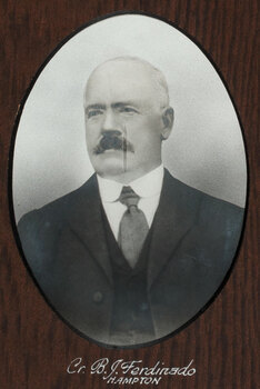 Black and white photograph of an oval portrait of a suited man with balding white hair and dark moustache