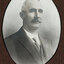 Black and white photograph of an oval portrait of a suited man with balding white hair and dark moustache