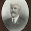 Black and white photograph of an oval portrait of a suited man with thick white hair and goatee.