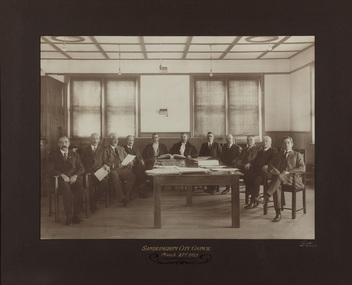 Gelatin silver photograph of a meeting with eleven men sitting on chairs around a large table