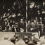 Sepia photograph of 2 men including a man in a top hat addressing a crowd. 