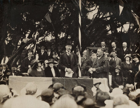 Sepia photograph of 2 men including a man in a top hat addressing a crowd. 