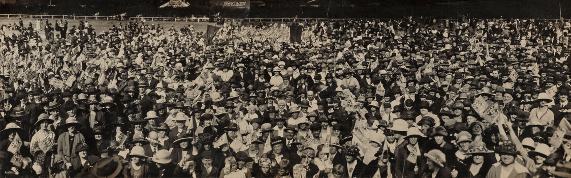 Panoramic sepia photograph of a large crowd of people on a football oval.