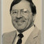 Black and white photograph of a photographic portrait of a man with dark hair and glasses in a suit and tie.