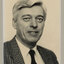 Black and white photographic portrait of a man with white hair in a checked suit.
