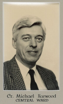 Black and white photographic portrait of a man with white hair in a checked suit.