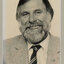 Black and white photographic portrait of a man with dark hair and grey beard wearing a suit and tie.