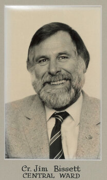 Black and white photographic portrait of a man with dark hair and grey beard wearing a suit and tie.