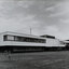 Black and white photograph of a modern office building, 2 stories high, with grass in front and clouds above.