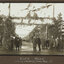 Black and white photograph of a street decorated with flags and lined with people