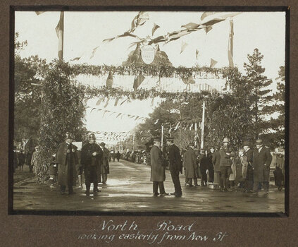 Black and white photograph of a street decorated with flags and lined with people