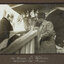 Black and white photograph of a man with white hair and a beard shaking hands with a man in a bowler hat. Behind them are flags