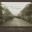 Black and white photograph of a street decorated with flags, lined with crowds of people