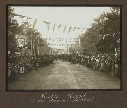 Black and white photograph of a street decorated with flags, lined with crowds of people