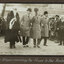 Black and white photograph of a man with white hair in mayoral robes standing next to 3 men with bowler hats, man in centre has his raised.