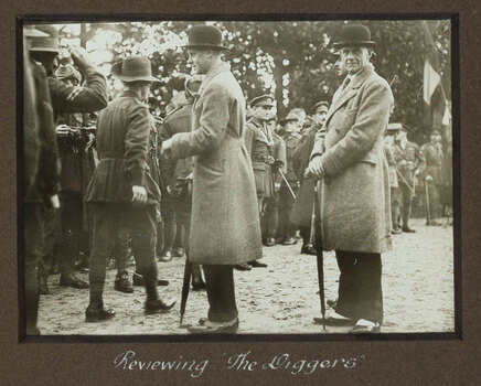 Black and white photograph of 2 men in bowler hats greeting a row of soldiers in uniform.