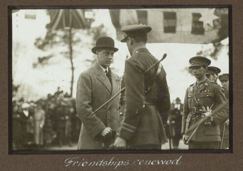 Black and white photograph of The Prince, in a bowler hat, shaking hands with a uniformed soldier