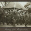 Black and white photograph of a large group of uniformed solders, a small building in background