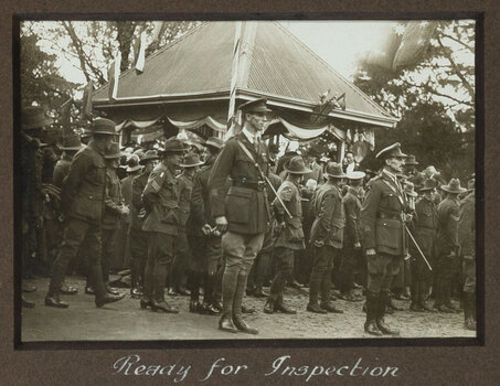 Black and white photograph of a large group of uniformed solders, a small building in background